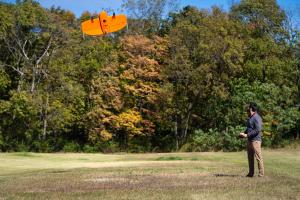 A man is seen flying a large, orange drone. 