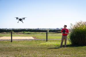 A man in a red shirt is seen flying a drone. 